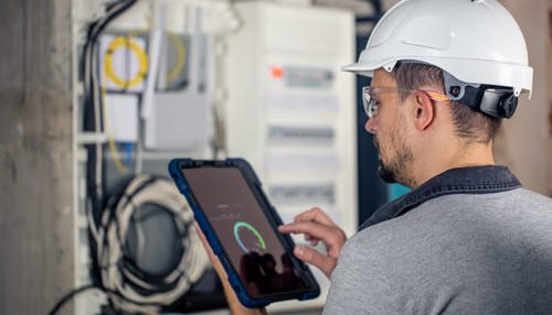 man-electrical-technician-working-switchboard-with-fuses-uses-tablet
